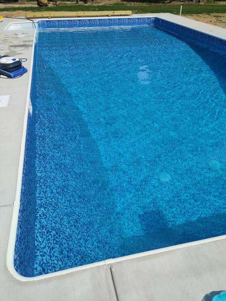 Rectangular blue swimming pool with white deck and grassy yard in the background