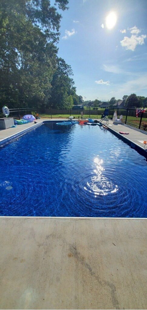 Sunny outdoor swimming pool with blue water, lounge chairs, and trees in the background
