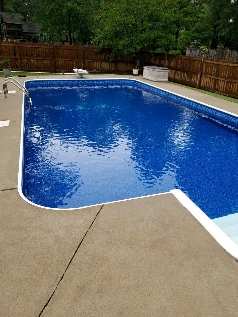 Backyard swimming pool with blue water, beige deck, and wooden fence