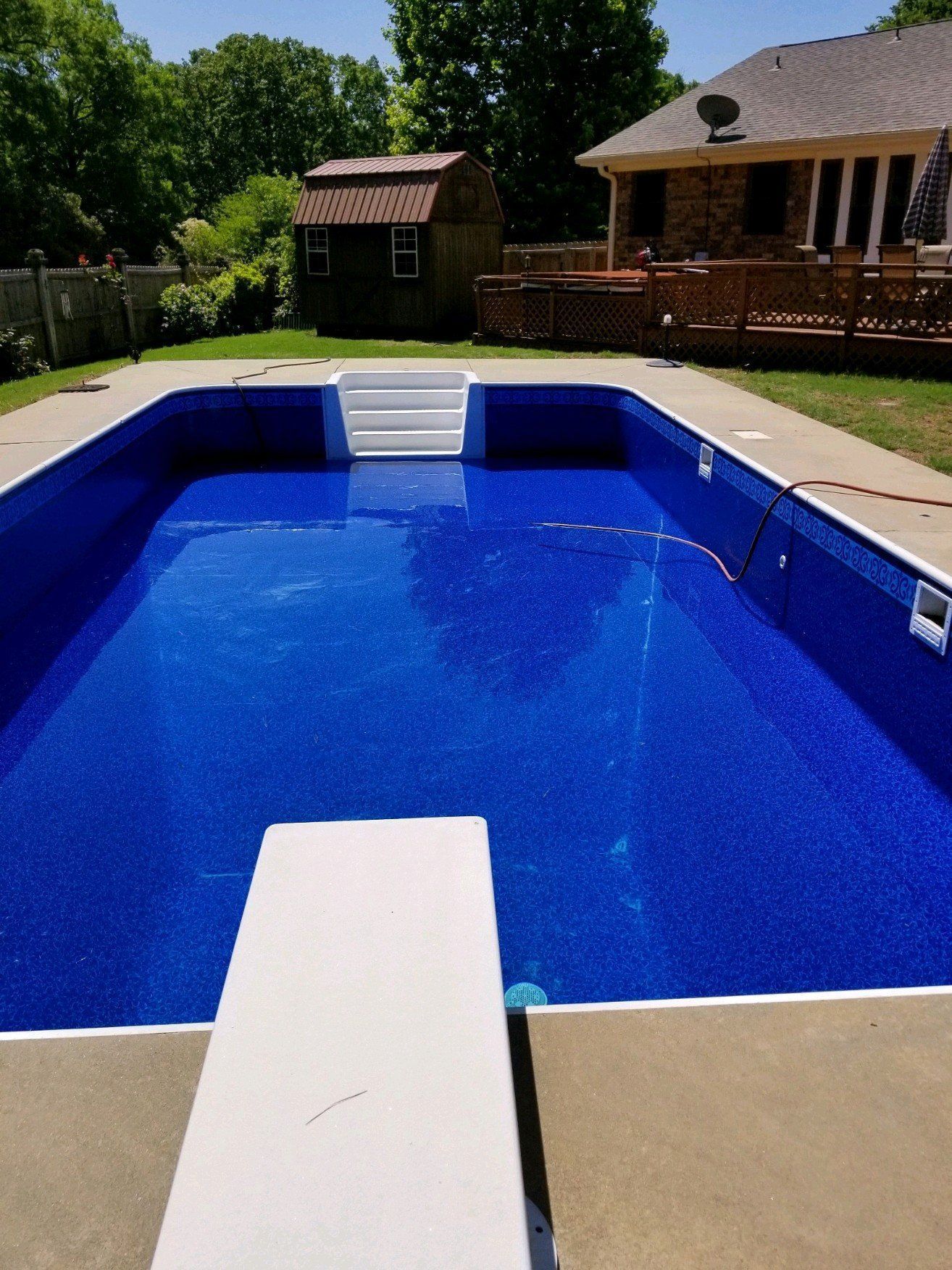 Backyard swimming pool with bright blue water, white diving board, and a house with patio in the background