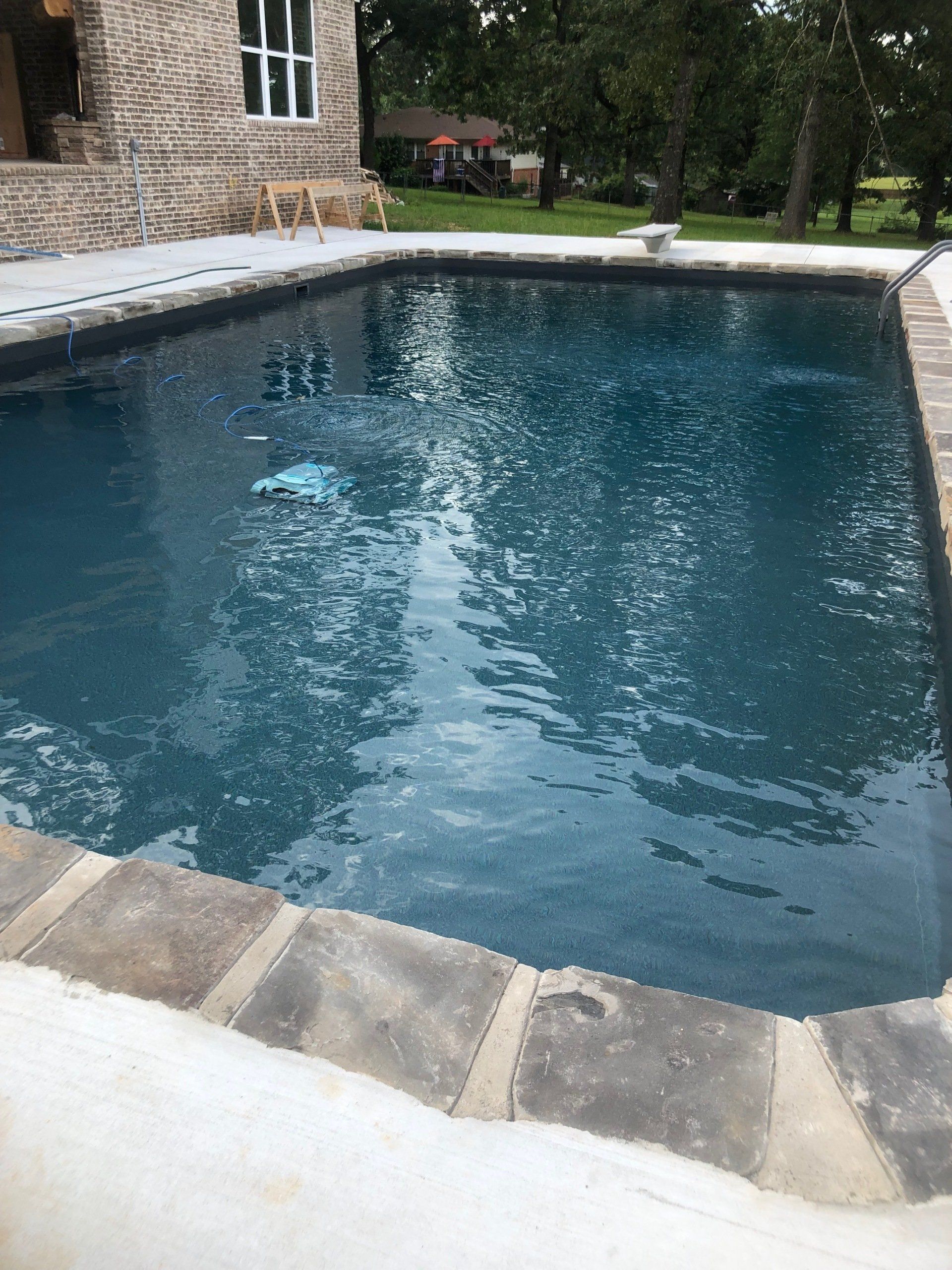 Backyard swimming pool with blue water beside a stone house and trees