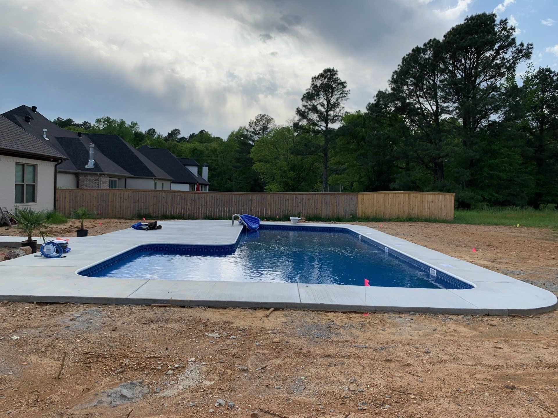 Backyard swimming pool with blue water, white deck, and a house and trees in the background