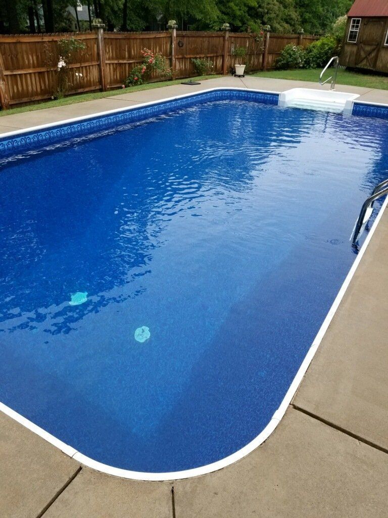 Blue backyard swimming pool with a wooden fence and tan deck.
