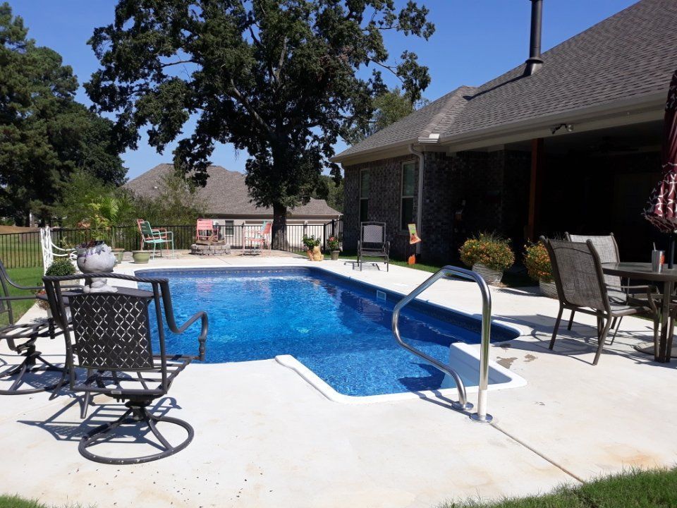 Backyard with a blue swimming pool, patio furniture, and a house under trees