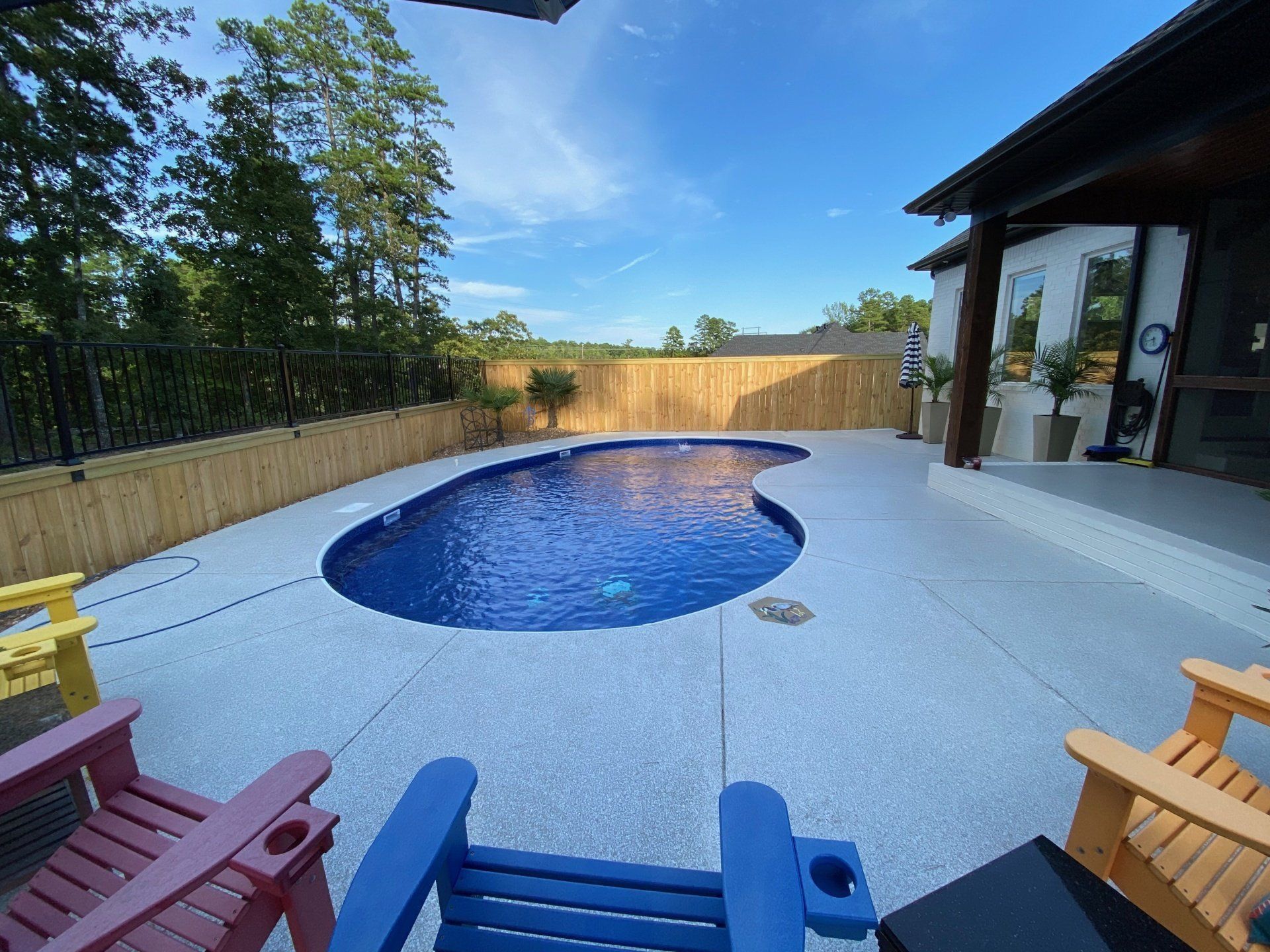 Backyard patio with blue swimming pool, colorful chairs, and a modern house beside a bamboo fence