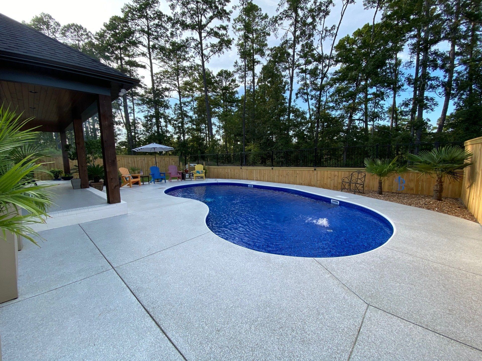 Backyard patio with a blue oval pool, white deck, and trees in the background