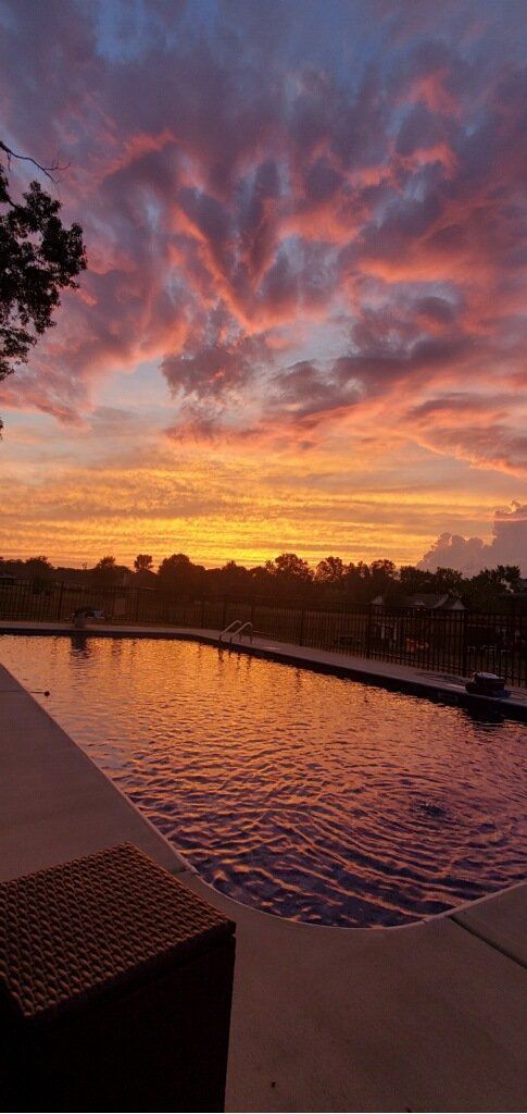 Sunset over a pool with rippling water, glowing orange and purple clouds above a waterfront horizon.