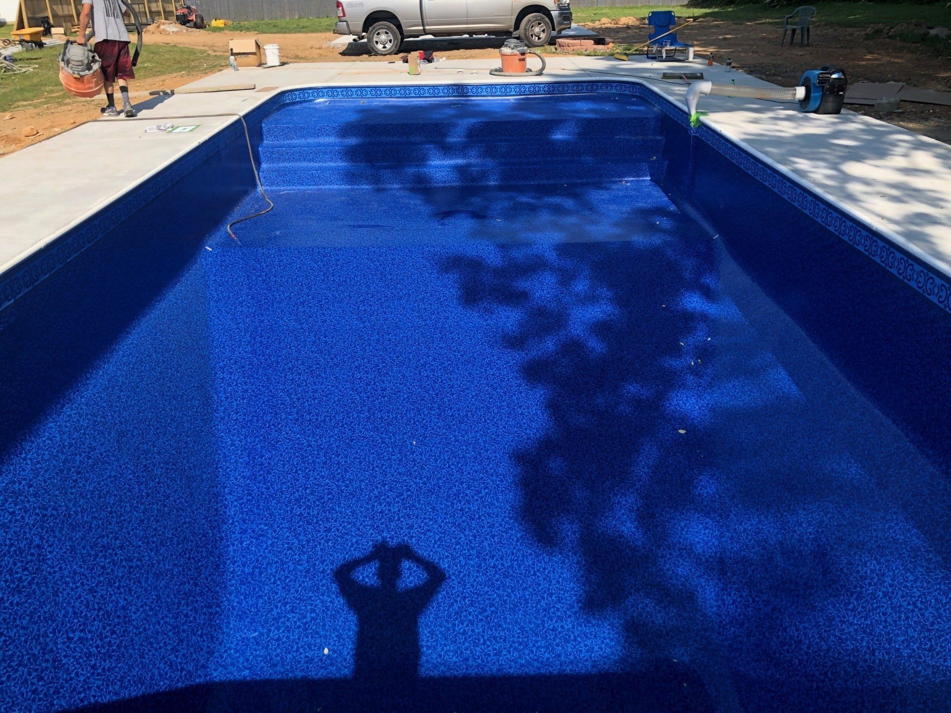 Blue-lined swimming pool with a person’s shadow reflected on the water and patio surroundings.