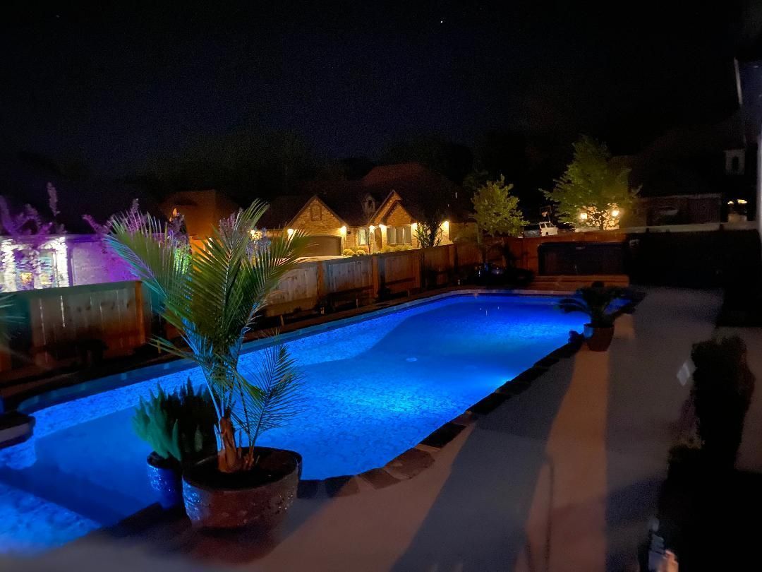 Blue-lit swimming pool at night with palm trees and resort buildings in the background