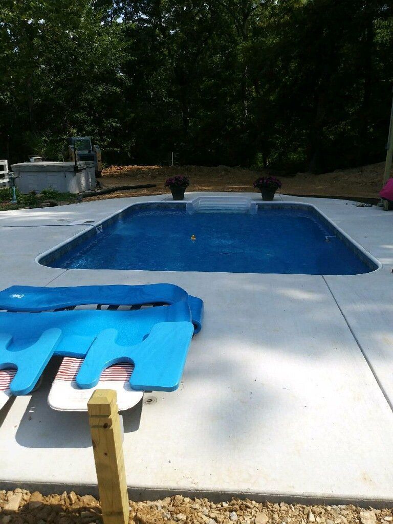 Backyard swimming pool with blue water, lounge chairs, and a concrete deck surrounded by trees