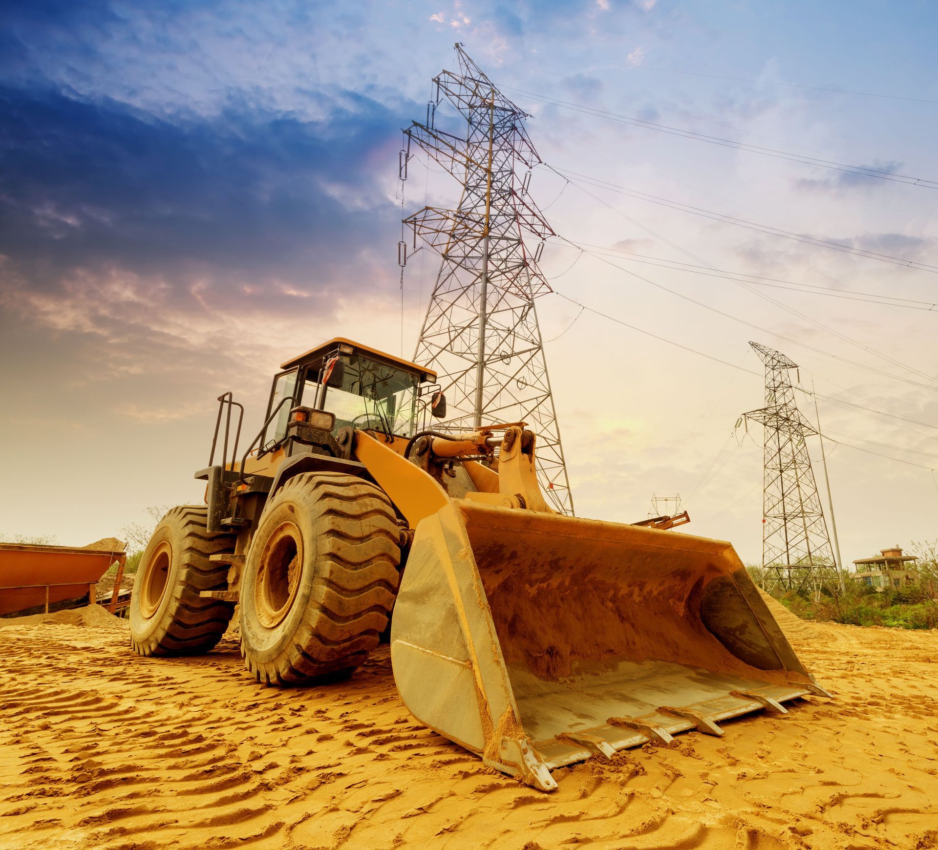 Bulldozer on construction site with power lines in the background under a cloudy sky.