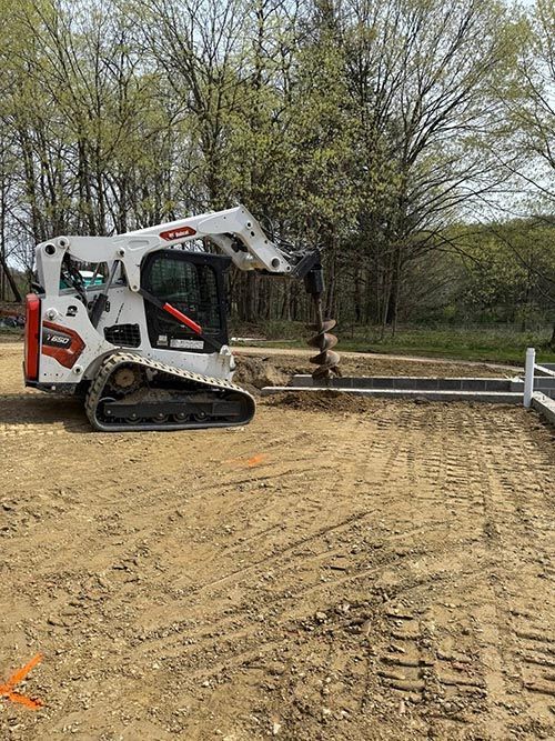 A white Bobcat skid-steer operating on a construction site. The machine is digging, with dirt and trees in the background.