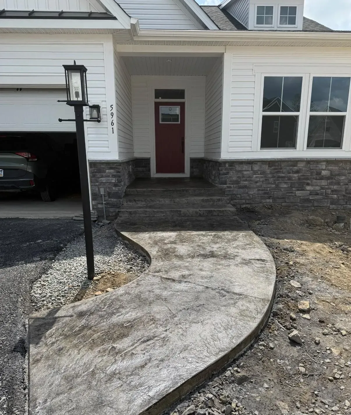 Concrete pathway leading to a white house with red door. Pathway curves, with a lamppost to the left.