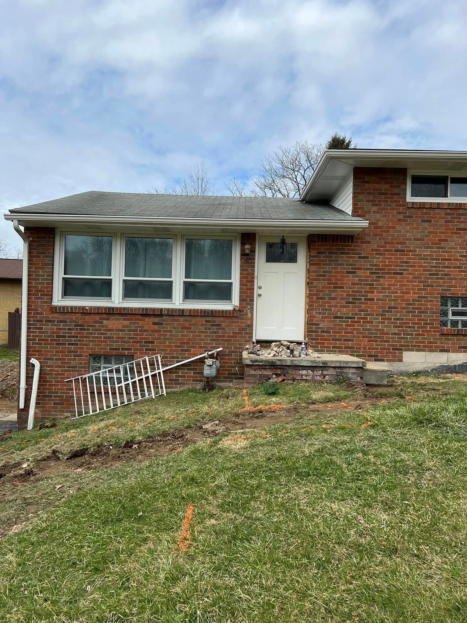 Red brick house with white trim and door on a grassy hill under a cloudy sky.