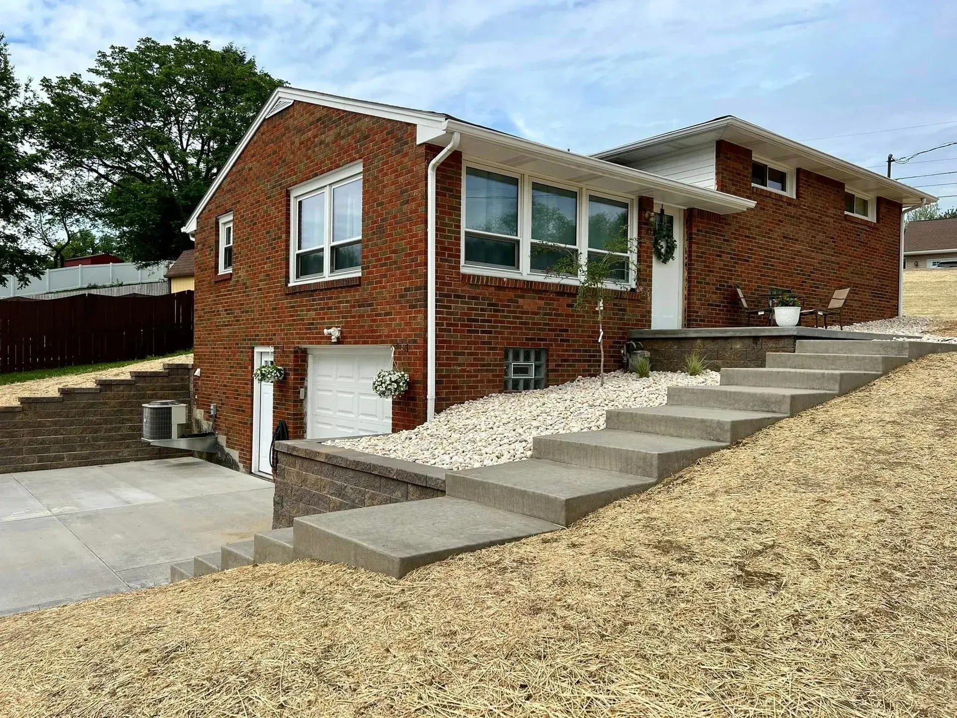 Brick house on a hillside with concrete steps leading to the front door and a garage.