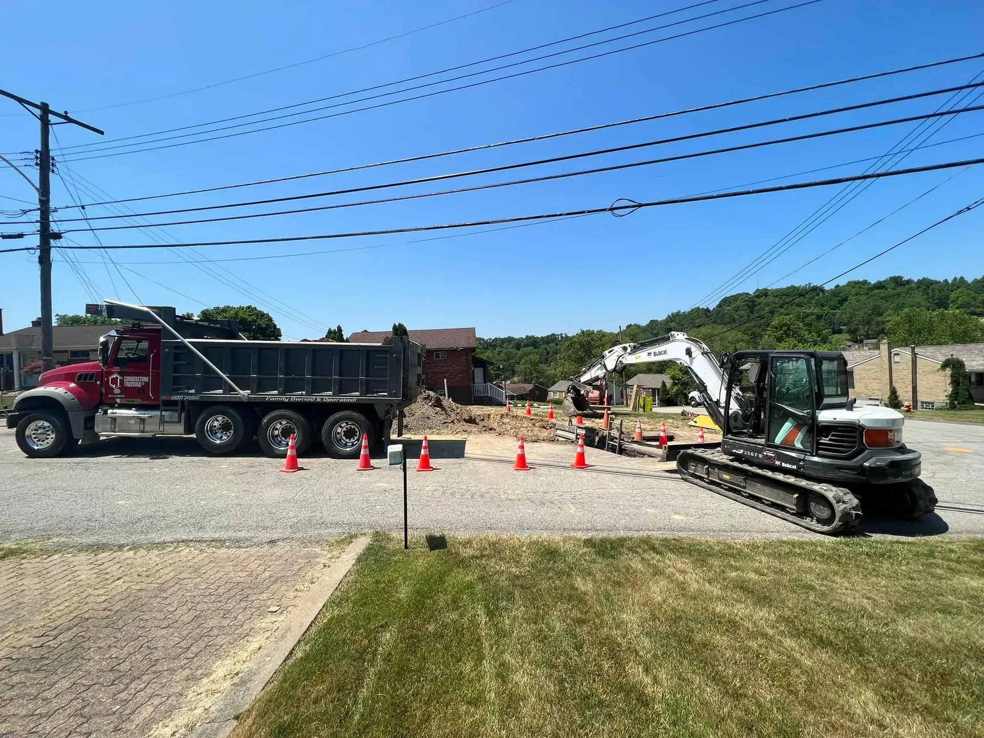 A dump truck and excavator working on a road, with traffic cones and a building in the background.