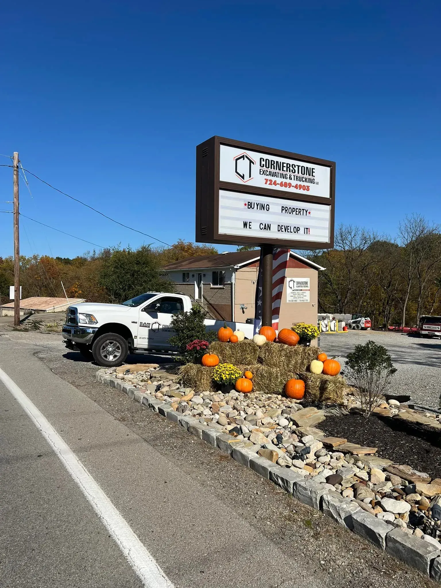 White truck parked in front of a business sign with pumpkins and fall decorations.