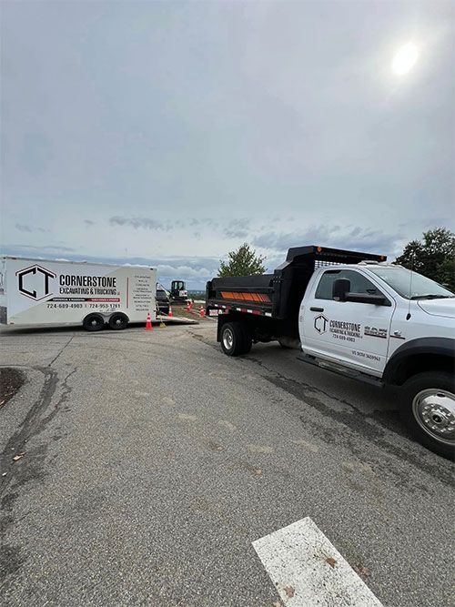 White dump truck and trailer with construction company logo parked at a construction site.