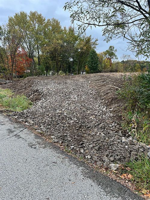 A graded lot covered in gravel next to a paved road, trees in the background.