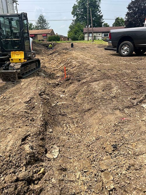 Construction site with an excavator digging a trench. A truck is parked to the right.