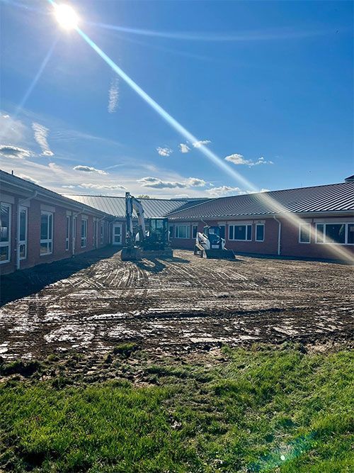 Construction site: earth movers between red buildings under a bright sun and blue sky.