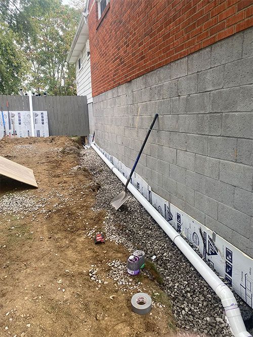 A side view of a house foundation with a drainage pipe and gravel, construction in progress.
