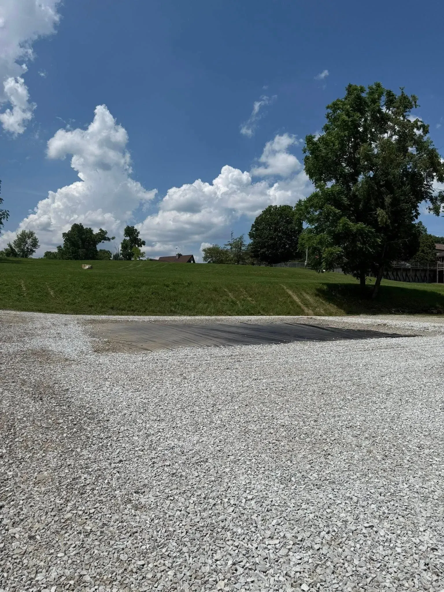 Gravel parking area with grassy hill, trees, and a cloudy blue sky.