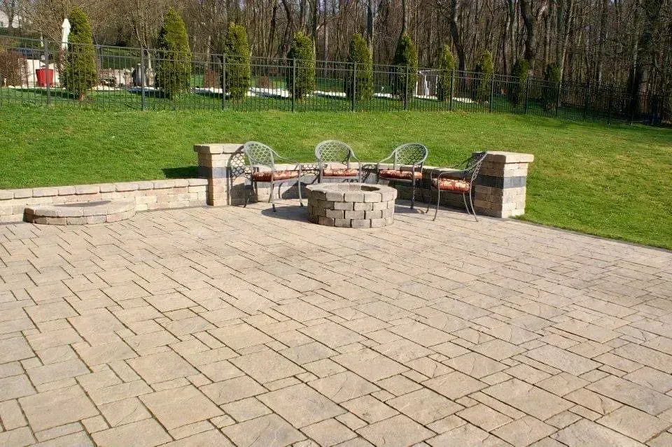 Patio with seating around a fire pit, on a sunny day with green lawn and trees in the background.
