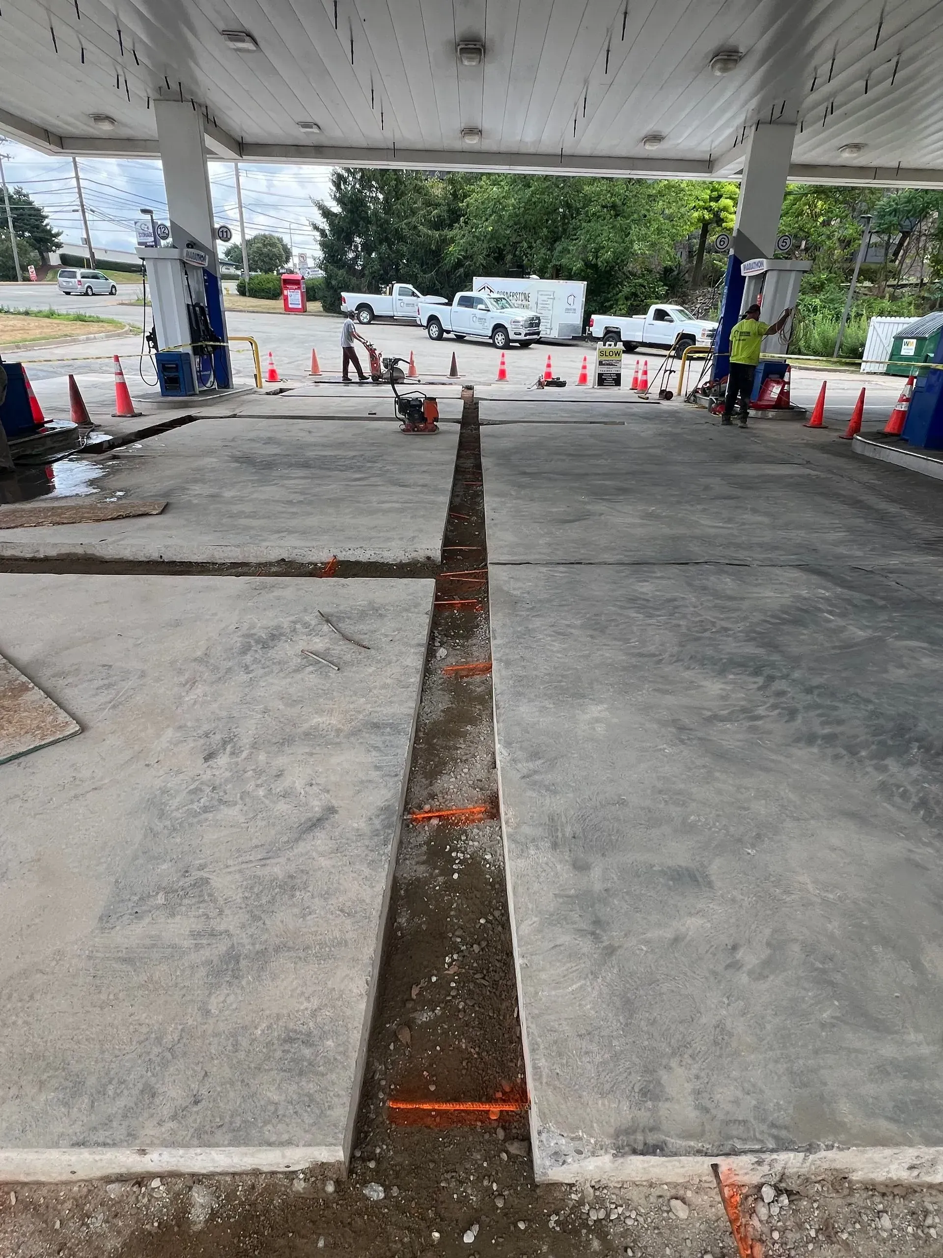 Gas station concrete cut for repair; orange cones and workers in background.
