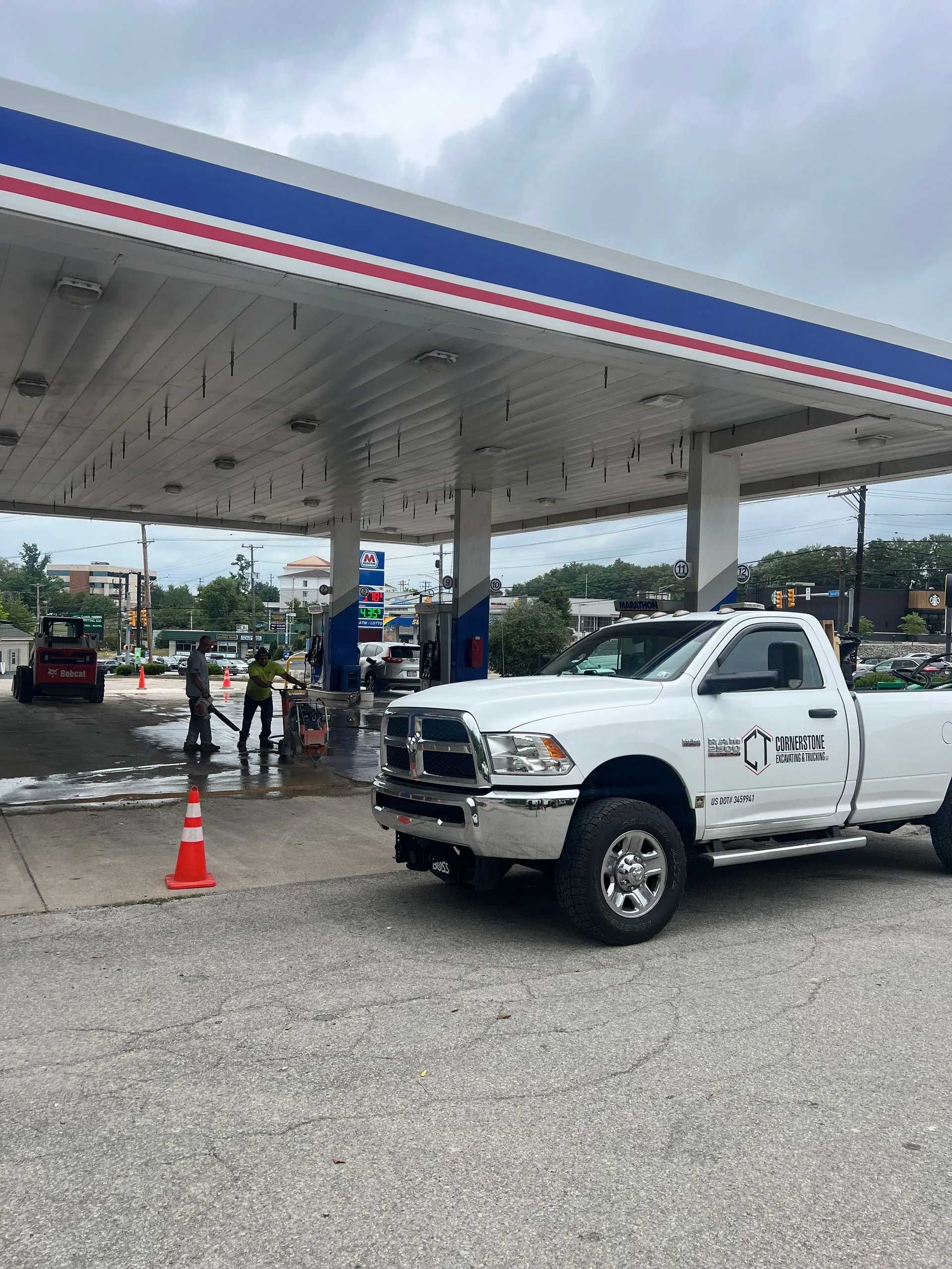 White pickup truck parked at gas station with workers cleaning; cloudy day.