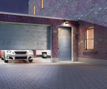 Car exiting partially open garage at night, brick building, lit door.