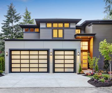 Modern home exterior with glass garage doors and landscaped front yard.