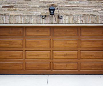 Brown paneled garage door under a brick wall with a black light fixture above.