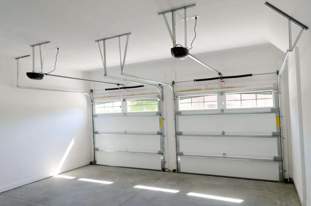 White garage interior with two doors. Overhead garage door openers and sunlight.