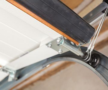 Garage door mechanism with cables, rollers, and track. White door panel.