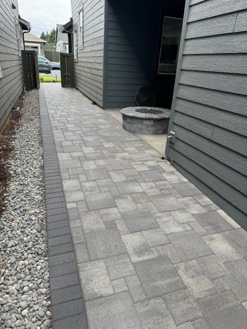 A brick walkway between two houses with a fire pit in the middle