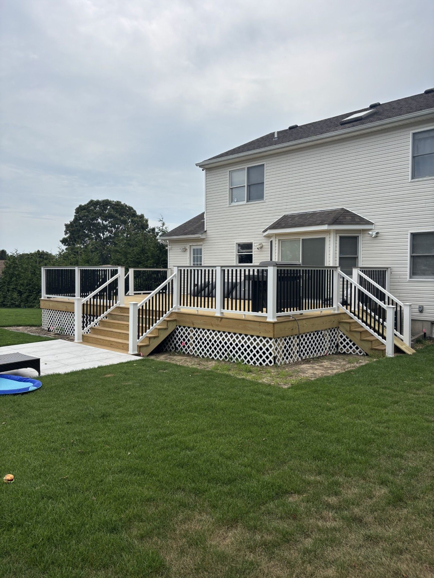 Backyard deck with white railings, stairs, and a two-story house in the background