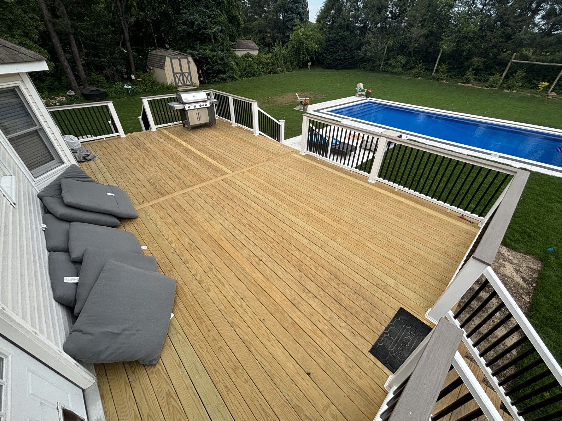 Wooden backyard deck with gray chairs overlooking a blue swimming pool and green lawn