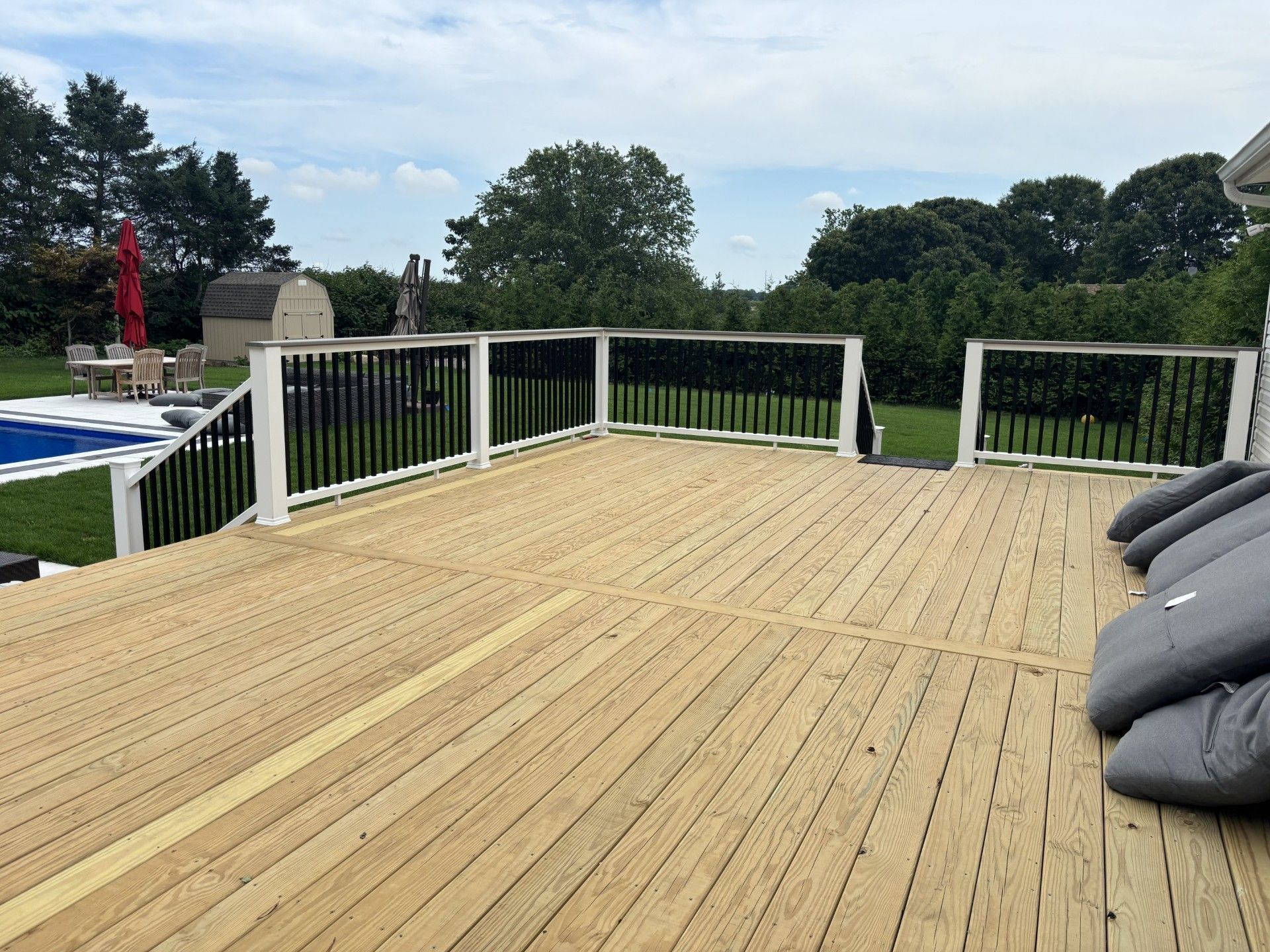 Wooden deck with white railing overlooking a backyard and trees under a cloudy sky