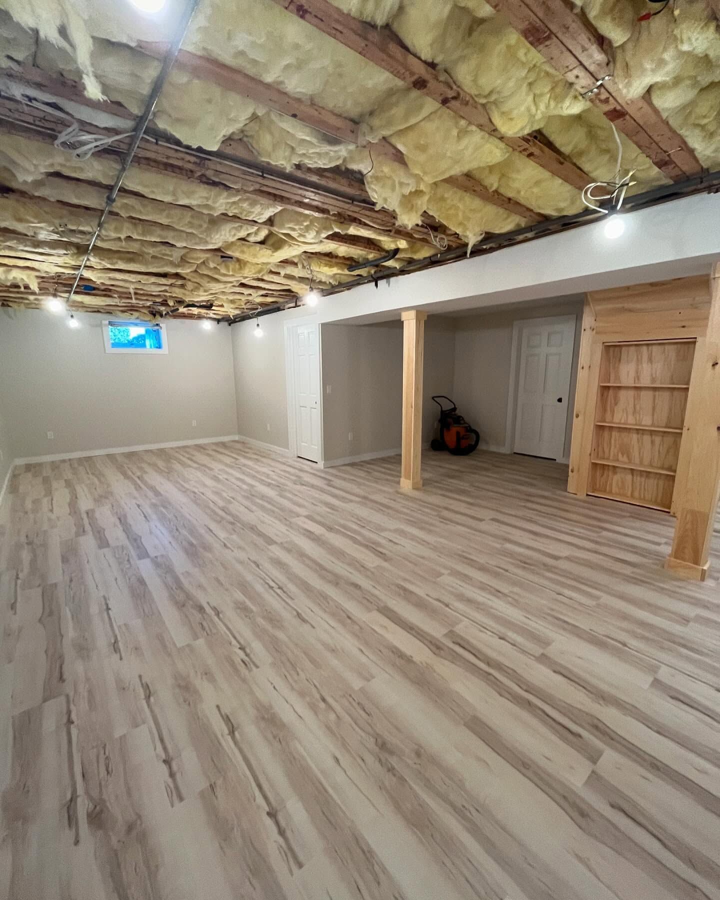 Unfinished basement room with exposed insulation, wood floor, and a small window.
