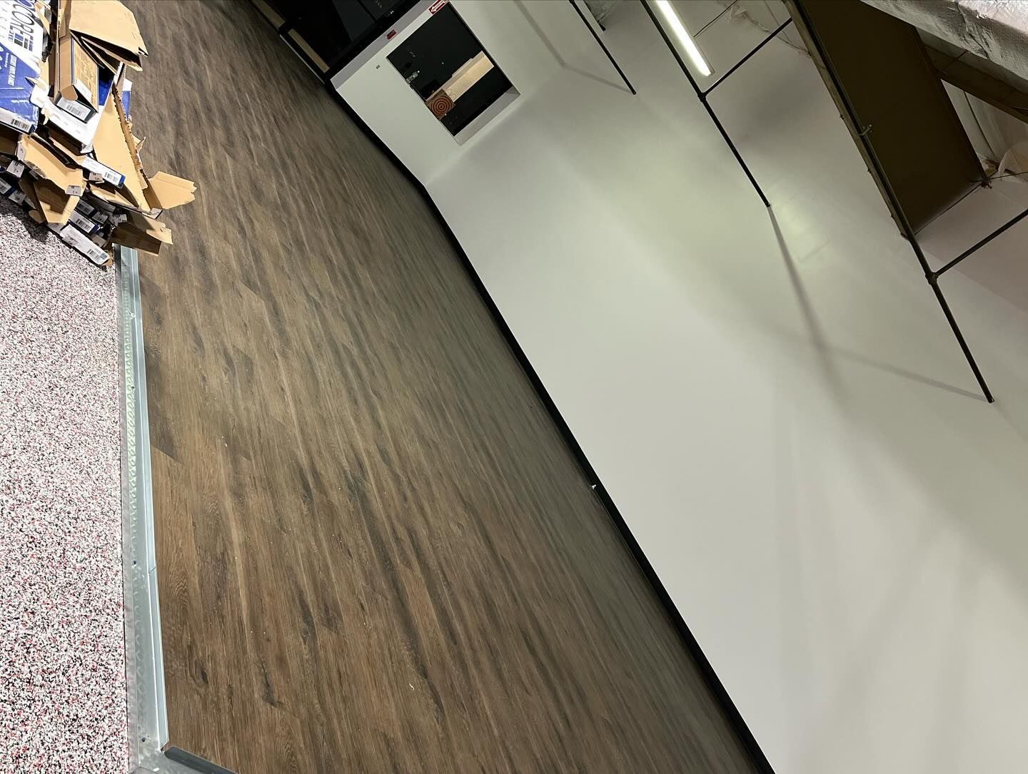 Empty office room with wood floor, white walls, and cardboard boxes near the corner