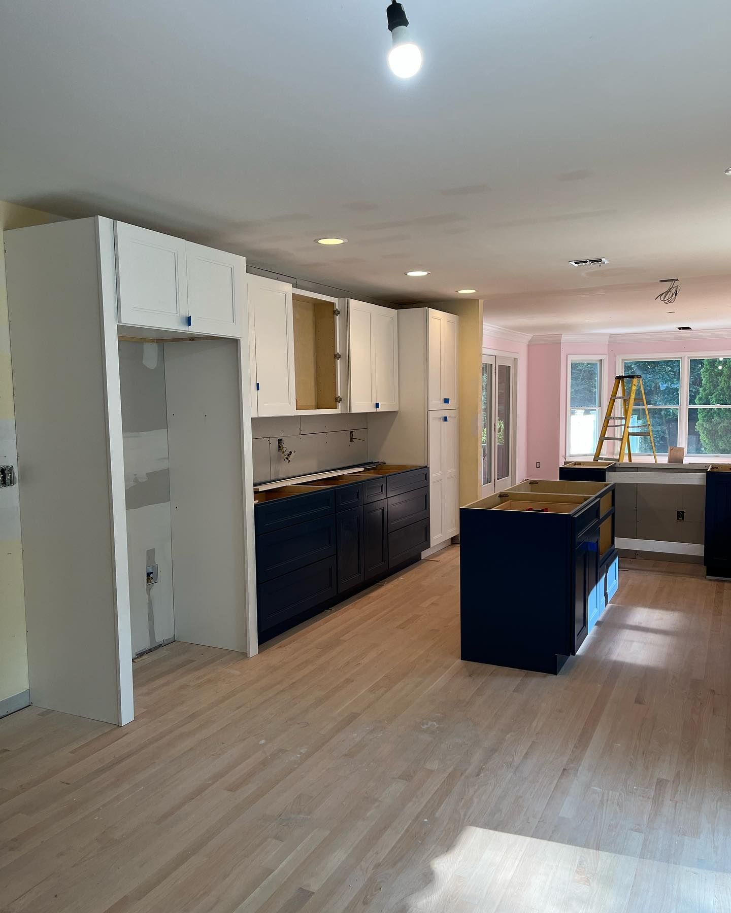 Bright modern kitchen with white cabinets, dark blue island, wood floor, and large windows.