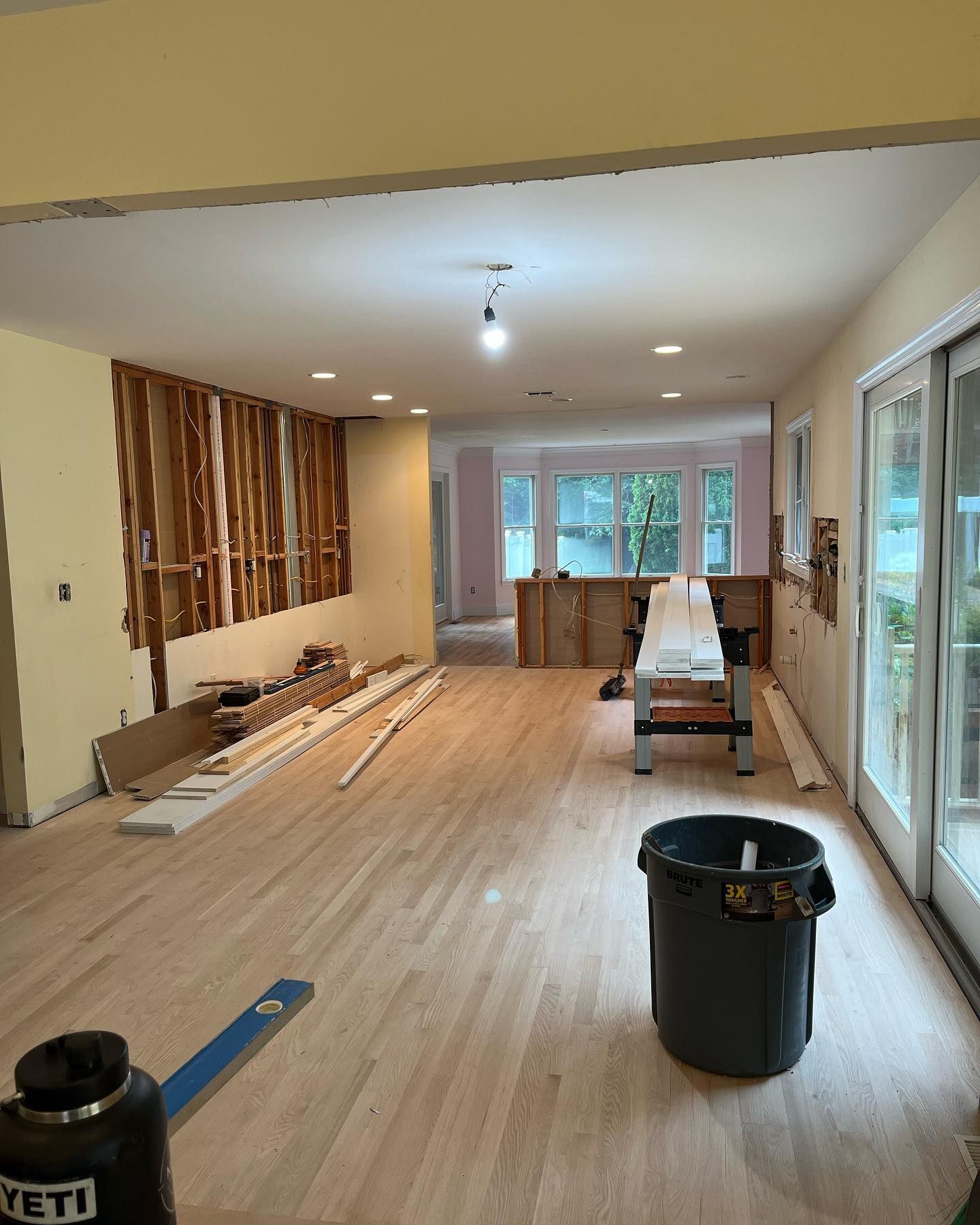 Empty room under renovation with wood flooring, tools, and sliding glass doors along the right wall