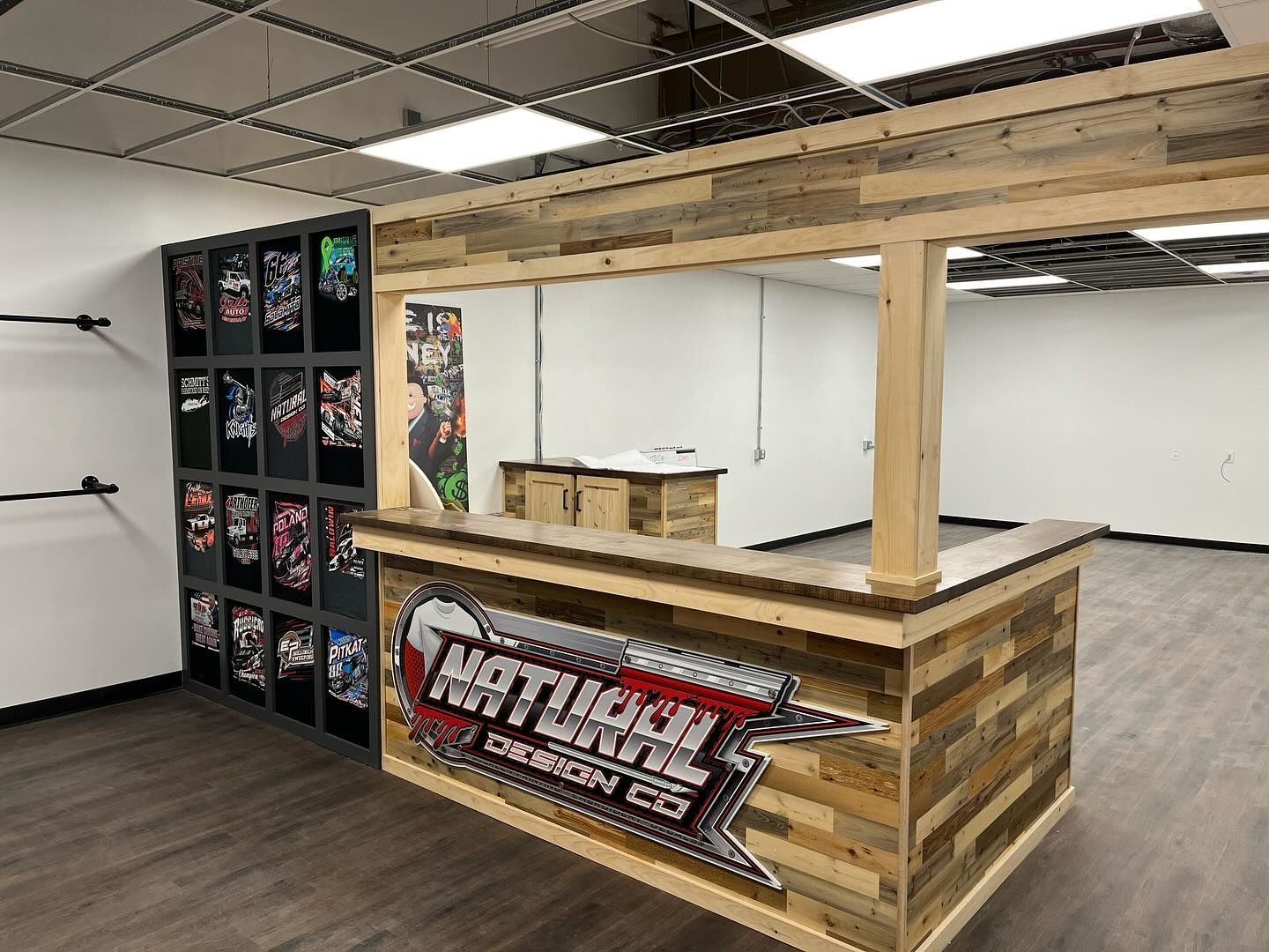 Wooden bar counter with overhead frame and back shelves in an empty retail space.