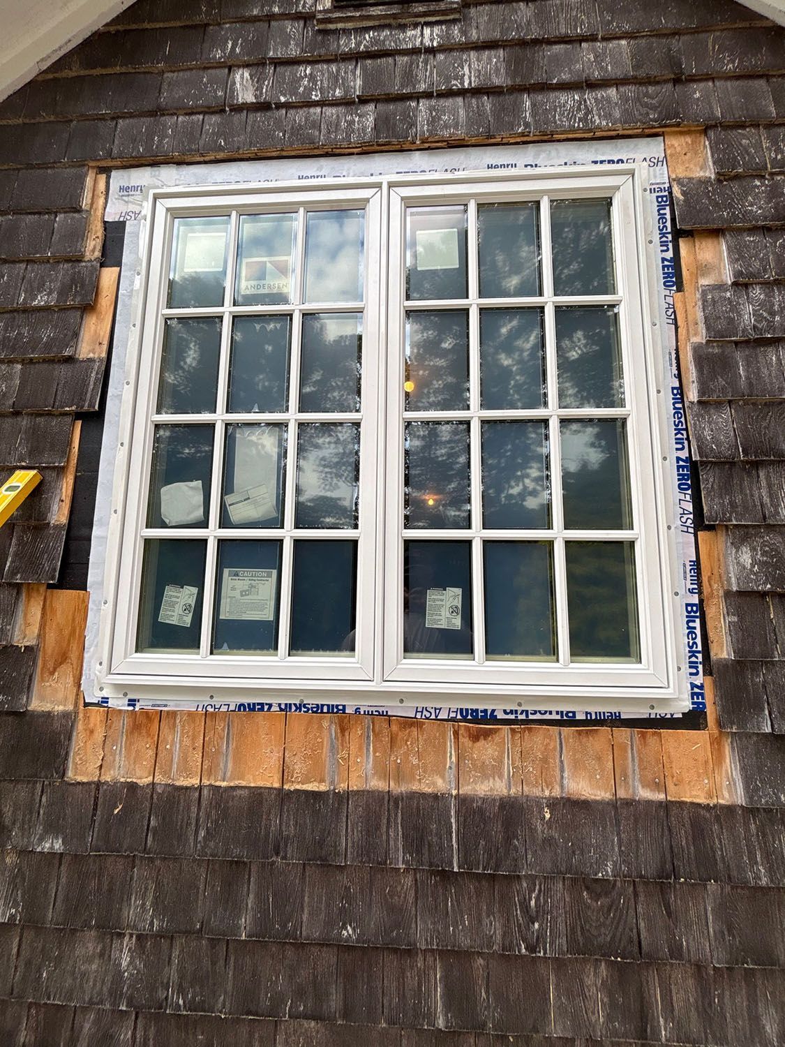 White-framed window in a shingled exterior wall with blue painter’s tape around the edges.