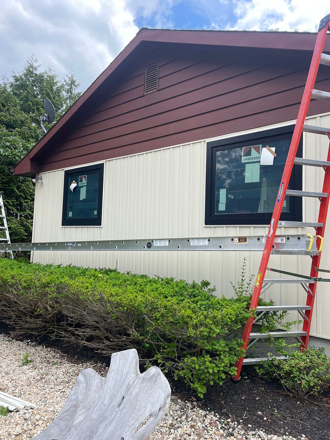 Red ladder beside a house with brown gable and white siding, viewed from the side.