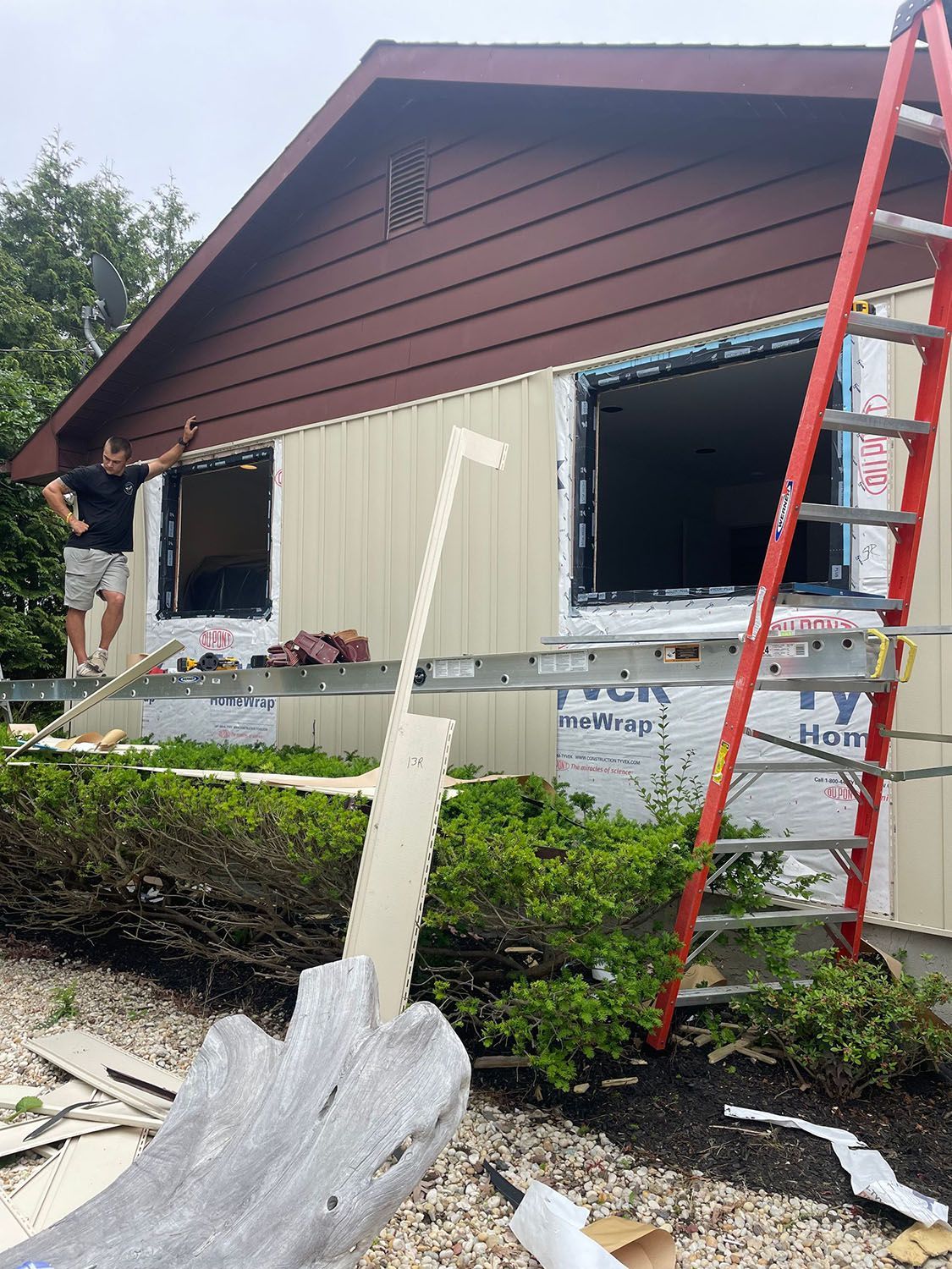 House exterior under renovation with workers, ladder, and siding panels removed.
