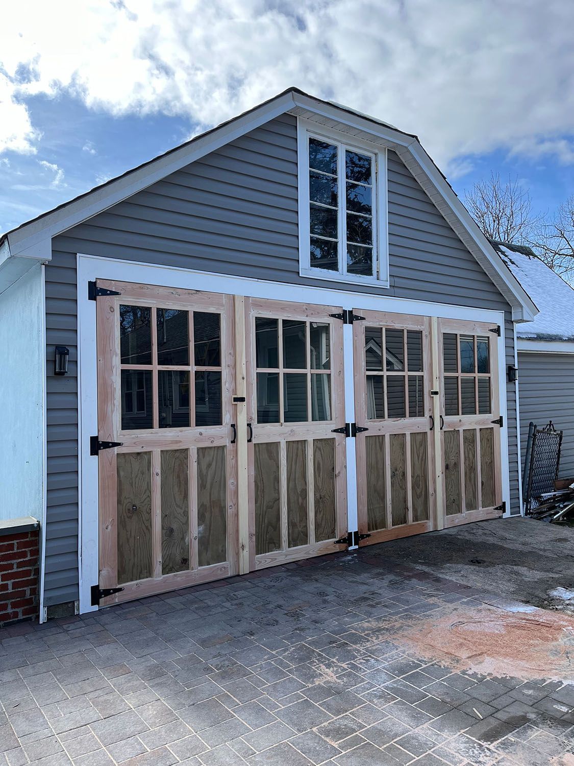 Small house exterior with unfinished double doors and windows under a gabled roof.
