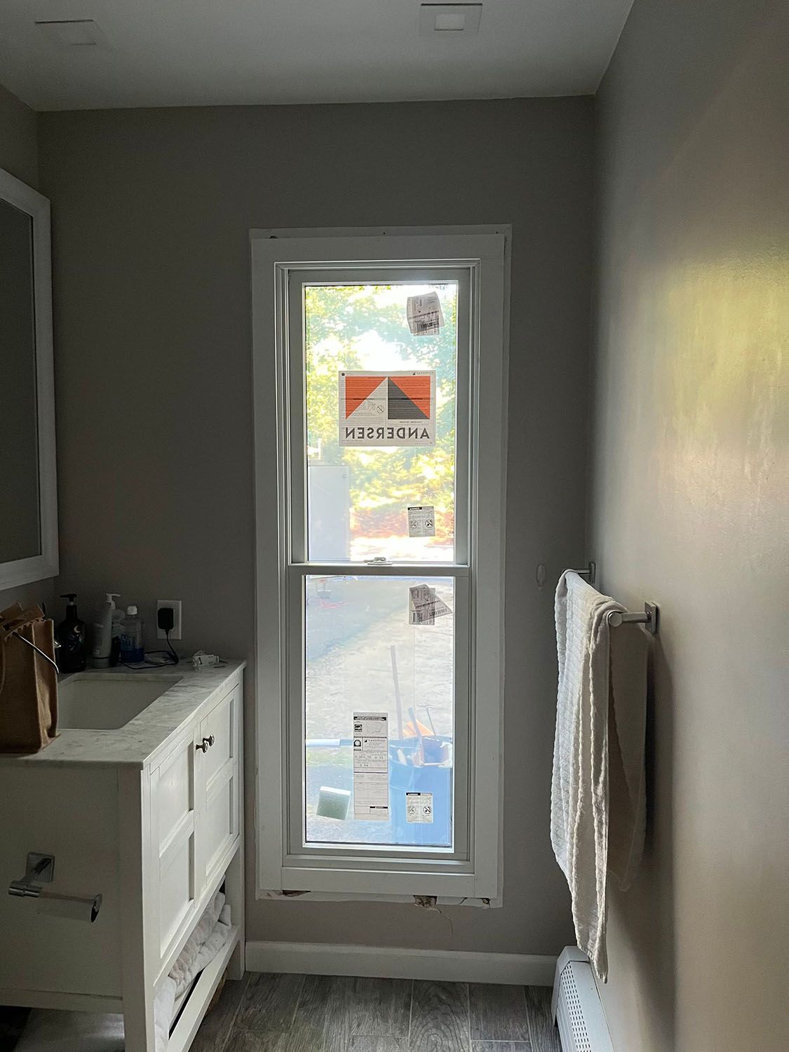 Narrow bathroom with gray walls, white dresser, and a small window above a towel rack.