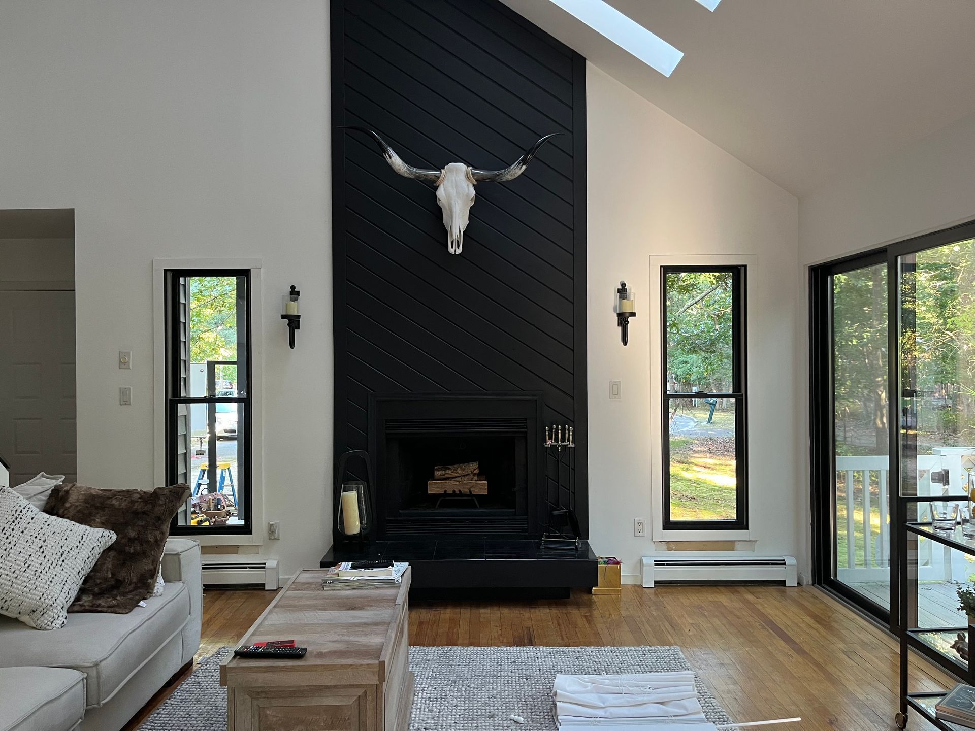 Modern living room with black fireplace, mounted skull, large windows, and neutral furniture.